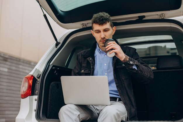 Uomo seduto nel bagagliaio della sua auto e lavorando al computer