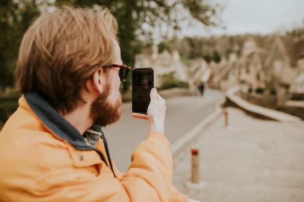 Uomo seduto su una panchina e scattare foto sul suo telefono nel villaggio