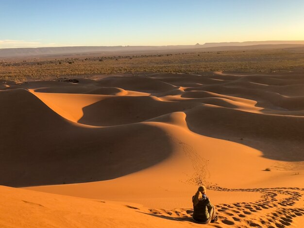 Uomo seduto sulle dune del sole in un deserto circondato da tracce