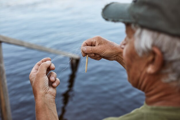 Uomo senior con i capelli grigi che indossa il berretto da baseball e la maglietta verde esca la canna da pesca, maschio anziano trascorrere del tempo vicino al fiume o al lago, con il resto all'aria aperta.