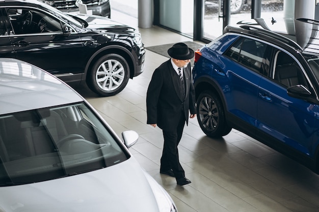 Uomo senior in una sala d'esposizione dell'automobile che sceglie un'automobile