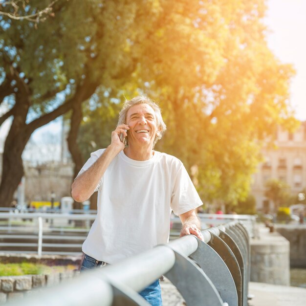 Uomo senior sorridente che sta nel parco che parla sul telefono cellulare