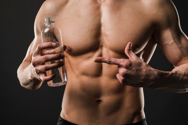 Uomo senza camicia atletico che indica alla bottiglia di acqua