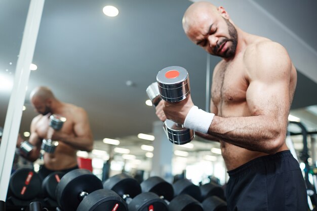 Uomo senza camicia che risolve con i pesi in palestra