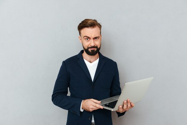 Uomo serio aggrottante le sopracciglia in vestito facendo uso del computer portatile isolato