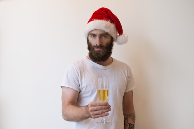 Uomo serio che porta il cappello di Santa e che tiene calice con champagne