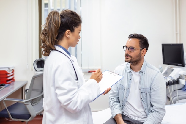 Uomo serio che si consulta con una giovane dottoressa medico alla riunione di controllo in ospedale Medico generico qualificato che fornisce consigli medici sanitari al paziente