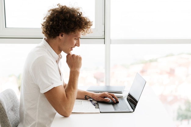 Uomo serio concentrato bello che per mezzo del computer portatile.