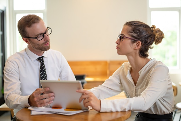 Uomo serio e donna di affari che lavorano al computer tablet in ufficio.