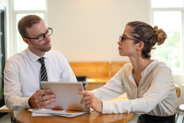 Uomo serio e donna di affari che lavorano al computer tablet in ufficio.