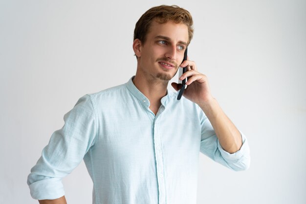 Uomo sicuro pensieroso in camicia blu che invita telefono cellulare.