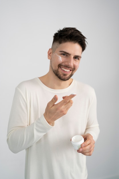 Uomo sorridente a colpo medio che applica la crema per il viso