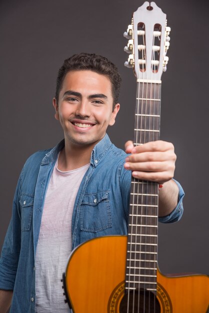 Uomo sorridente a suonare la chitarra su sfondo scuro. Foto di alta qualità