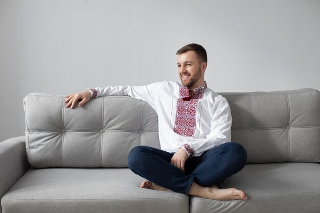 Uomo sorridente a tutto campo con camicia ucraina sul divano