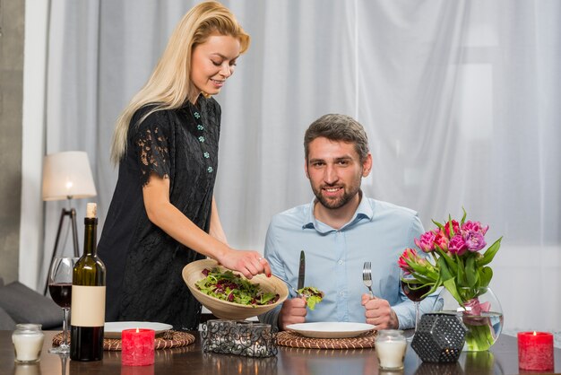 Uomo sorridente al tavolo vicino donna con ciotola di insalata