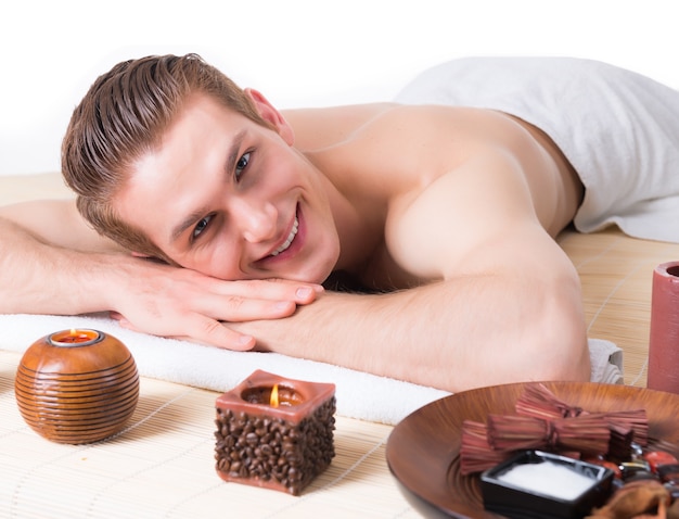 Uomo sorridente bello sdraiato sui banchi di massaggio presso il salone spa e rilassarsi. Concetto di trattamento di bellezza.