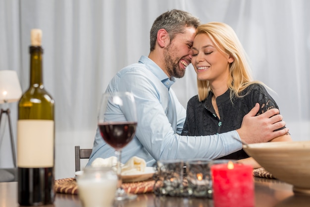 Uomo sorridente che abbraccia donna allegra al tavolo