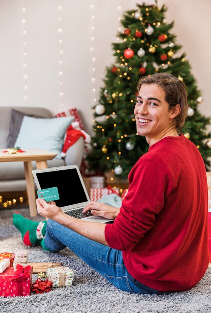 Uomo sorridente che compera online con il computer portatile
