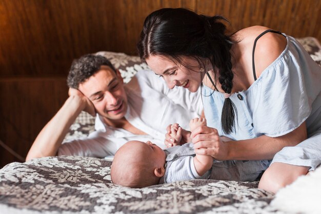 Uomo sorridente che esamina il suo bambino che gioca con la madre sul letto