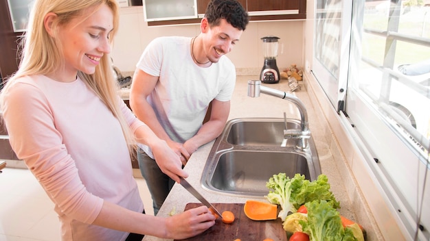 Uomo sorridente che esamina le fette di taglio della donna di carota nella cucina