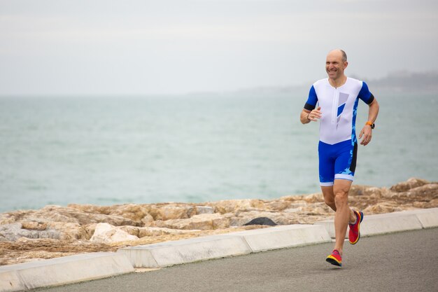 Uomo sorridente che funziona sulla costa del mare