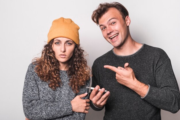 Uomo sorridente che indica dito al termometro della holding della donna malata