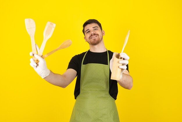 Uomo sorridente che mostra i suoi cucchiai di legno alla telecamera su giallo.