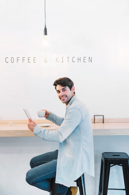 Uomo sorridente che si siede con la tazza e la compressa