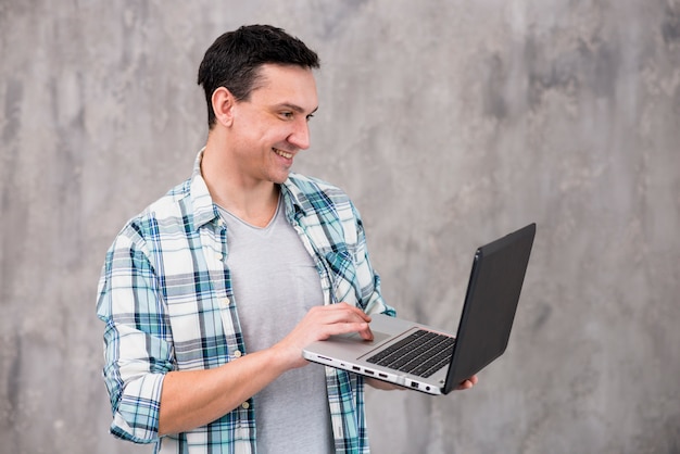 Uomo sorridente che sta e che per mezzo del computer portatile