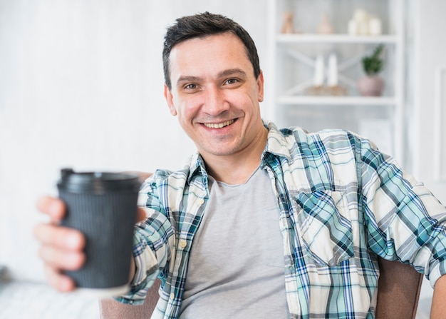 Uomo sorridente che tiene tazza della bevanda sulla sedia a casa