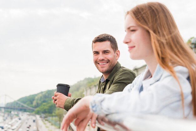 Uomo sorridente che tiene tazza monouso guardando la sua ragazza