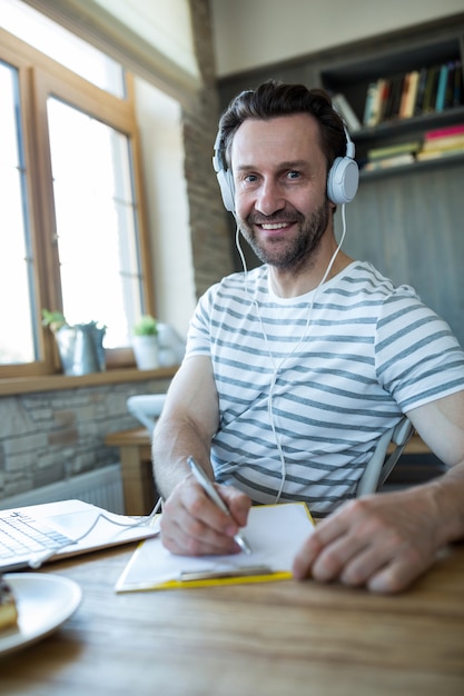 Uomo sorridente con le cuffie scrivendo nel suo diario a negozio di caffè