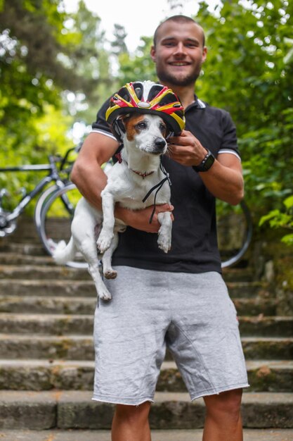 Uomo sorridente con un cane che si rilassa in un parco primaverile dopo il ciclismo.