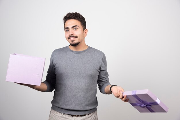 Uomo sorridente con una scatola viola aperta su un muro bianco.