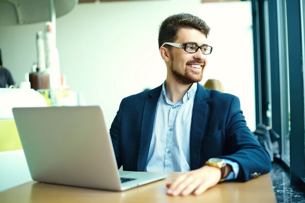 Uomo sorridente dei pantaloni a vita bassa di giovane modo nel caffè della città durante l'ora di pranzo con il taccuino in vestito