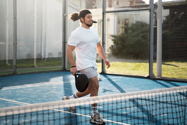 Uomo sorridente del colpo pieno che gioca a paddle tennis