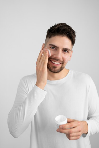 Uomo sorridente di vista frontale che applica crema per il viso