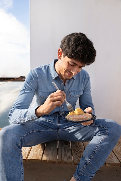 Uomo sorridente di vista frontale che mangia all'aperto