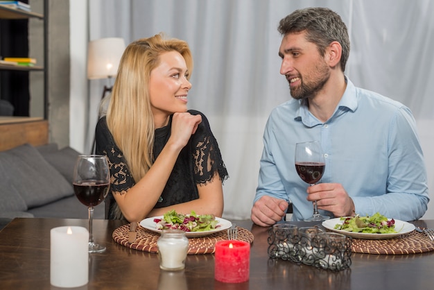 Uomo sorridente e donna allegra vicino a piatti e bicchieri al tavolo