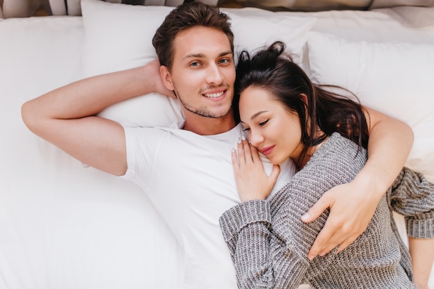 Uomo sorridente in posa a letto con la moglie che dorme sul petto