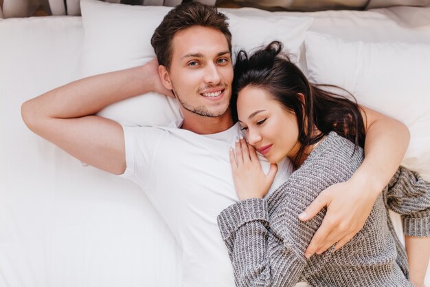 Uomo sorridente in posa a letto con la moglie che dorme sul petto