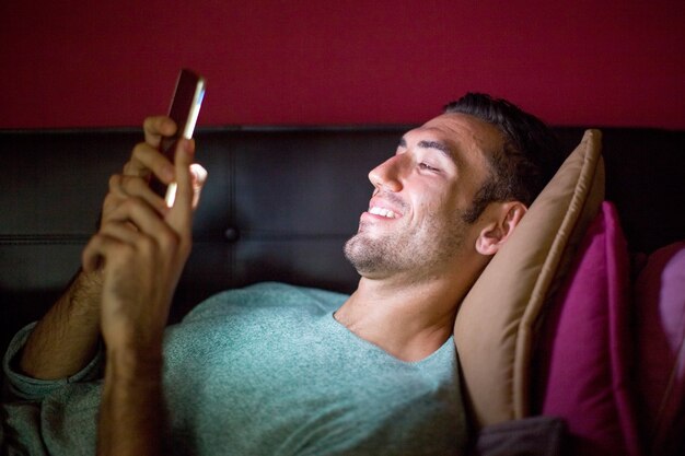 Uomo sorridente utilizzando smartphone sul divano a notte