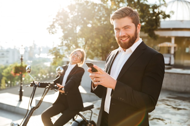 Uomo spensierato di affari che posa all'aperto facendo uso del telefono