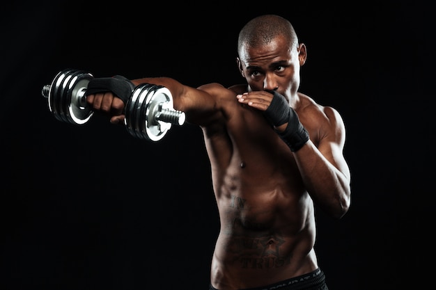Uomo sportivo afroamericano in posa come una lotta con manubri