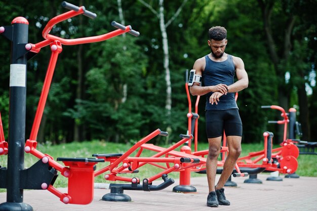 Uomo sportivo atleta maschio afroamericano con custodia per braccio sportivo da corsa per telefono cellulare in posa contro simulatori di allenamento in strada