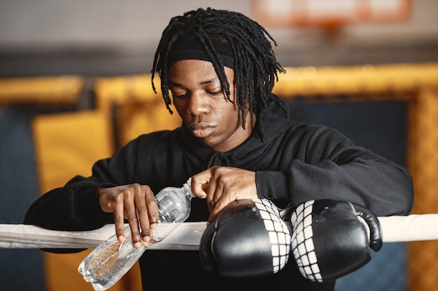 Uomo sportivo boxe. Foto del pugile su un anello. Uomo afroamericano con bottiglia d'acqua.