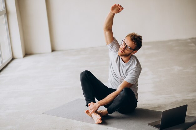 Uomo sportivo che guarda tutorial e pratica yoga sul tappetino