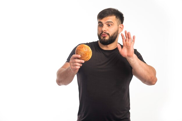 Uomo sportivo in camicia nera che tiene una ciambella e che rifiuta di mangiare.