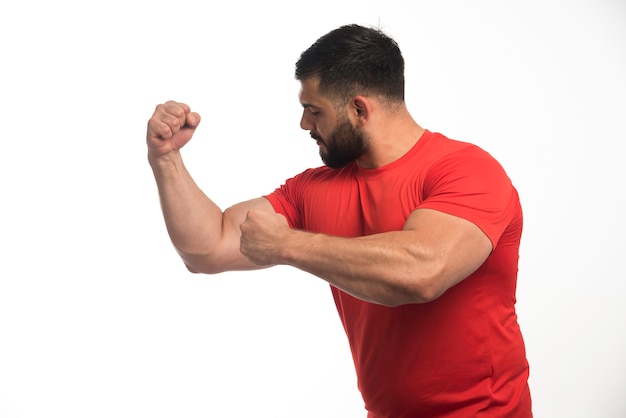 Uomo sportivo in camicia rossa che dimostra i suoi muscoli del braccio.