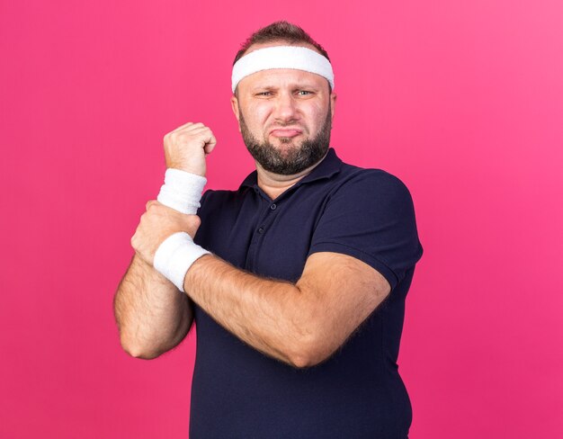 uomo sportivo slavo adulto dolorante che indossa fascia e braccialetti che tengono la mano isolata sulla parete rosa con spazio copia